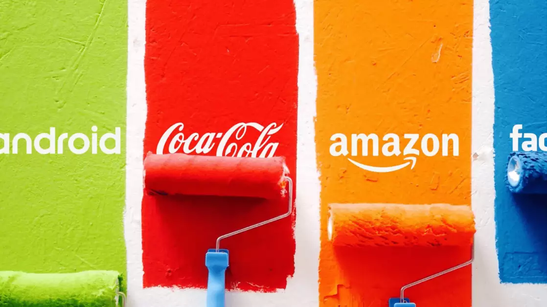 Três rolos de pintura aplicam cores vibrantes em uma parede, cada um associado a uma marca famosa: verde para Android, vermelho para Coca-Cola, laranja para Amazon e azul para Facebook. A psicologia das cores é evidente aqui, pois cada tonalidade influencia a percepção do público – o verde transmite inovação, o vermelho desperta emoções intensas, o laranja remete à criatividade e o azul gera confiança.