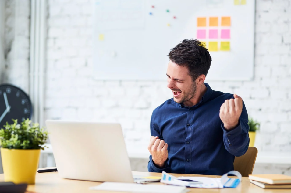 Homem comemorando sucesso em frente ao notebook, demonstrando satisfação e resultado positivo após aquisição ou produto Infoprodutos.