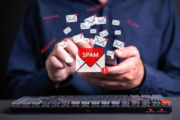 Um homem segurando um celular enquanto ícones de e-mails aparecem com alertas de "spam", "hacker" e "phishing". A imagem destaca a importância das boas práticas no E-mail Marketing para evitar que mensagens sejam consideradas spam e garantir altas taxas de entrega.