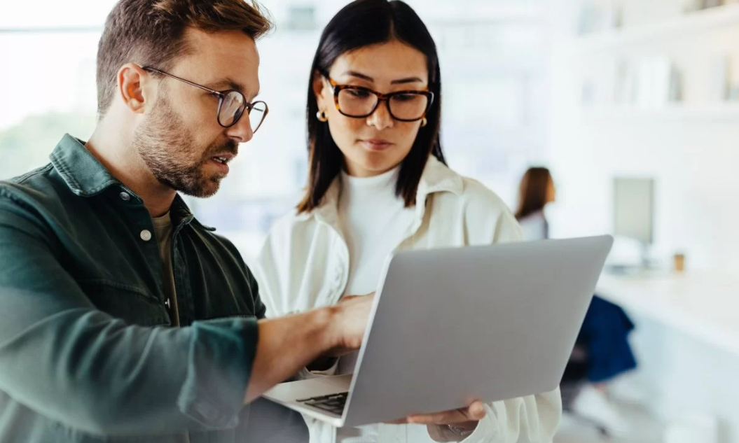 Professores discutindo um conteúdo de um curso online enquanto visualizam as informações em um laptop. Ambos estão imersos na explicação e análise de como usar ferramentas digitais para ensinar de maneira eficaz