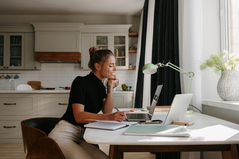 Mulher trabalhando remotamente em um laptop na mesa de sua cozinha, ilustrando a possibilidade de ganhar dinheiro online a partir do conforto de casa.