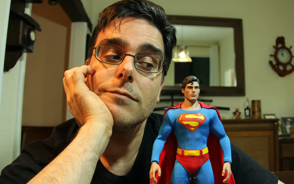Homem pensativo ao lado de boneco do Superman, contemplando alternativas de renda extra para superar desafios financeiros. A figura do super-herói simboliza o potencial de transformação quando se descobre novas formas de aumentar os rendimentos com trabalhos paralelos.