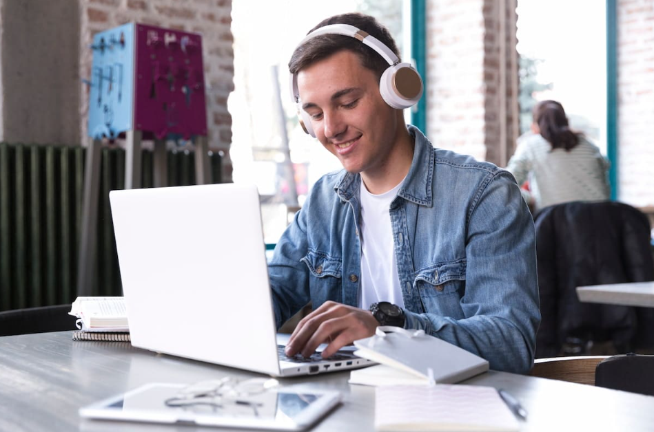 Jovem trabalhando em um notebook com fones de ouvido, representando oportunidades digitais sobre como ganhar dinheiro em casa.