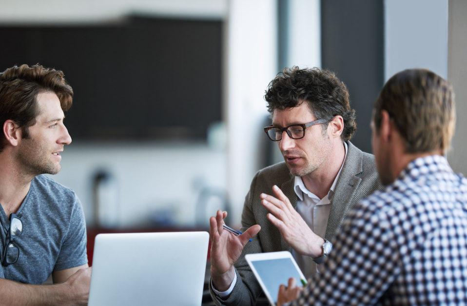 Três homens conversando seriamente em uma reunião com laptop e tablet, demonstrando networking estratégico entre empreendedores.