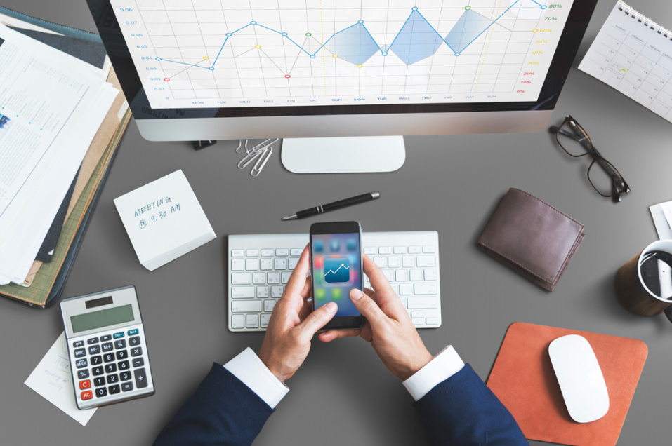 Pessoa segurando um celular com gráfico de vendas, em frente a um computador com dashboard de desempenho, representando análises e estratégias de como vender de forma inteligente e orientada por dados. Ideal para conteúdos sobre vendas digitais, funis e performance.