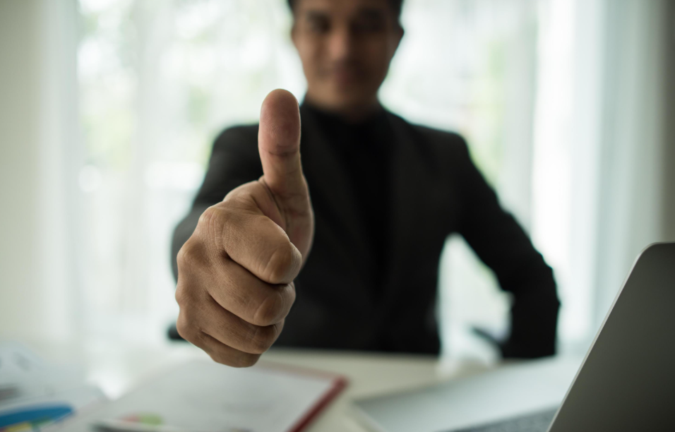 Homem de negócios fazendo sinal de positivo com o polegar em destaque, transmitindo confiança e aprovação, representando sucesso e eficácia ao aplicar estratégias sobre como vender com resultados.