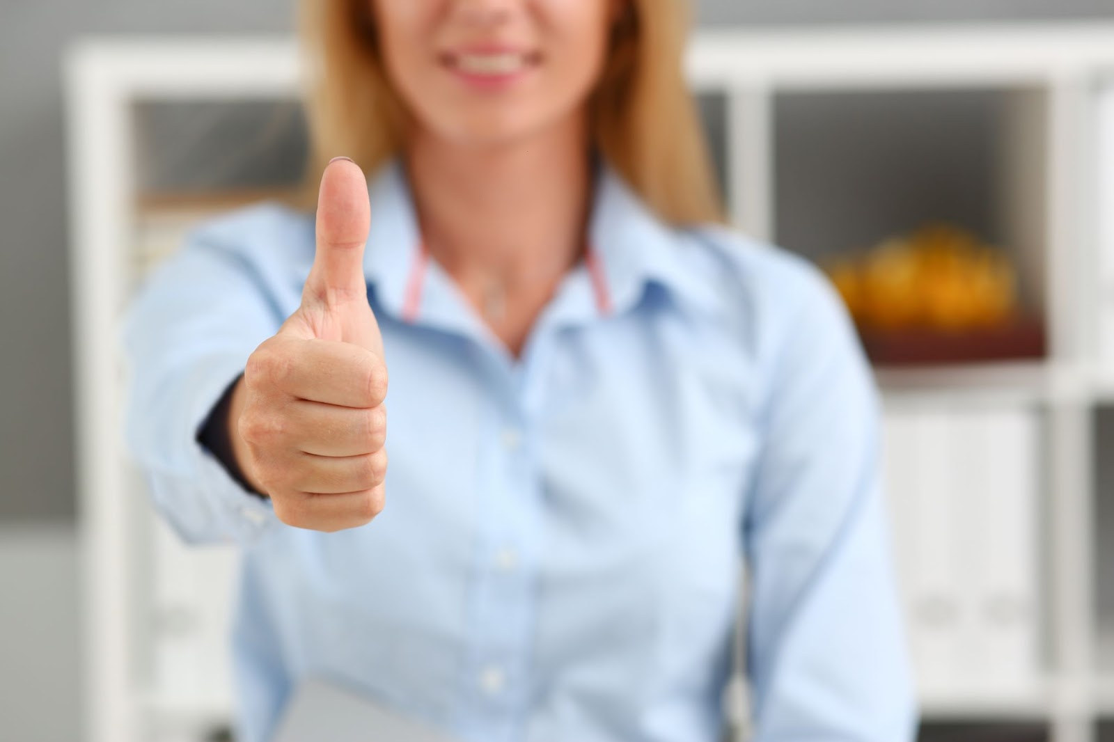 Mulher sorridente fazendo sinal de positivo com o polegar, simbolizando aprovação e confiança, elementos essenciais para um branding eficaz e bem-sucedido.
