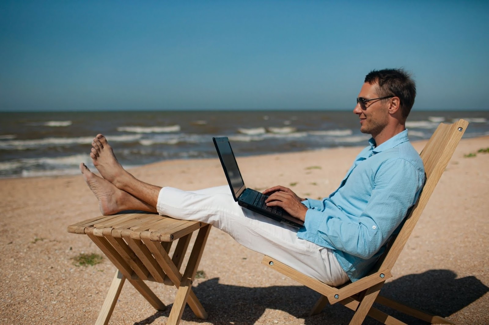 Homem relaxado trabalhando com notebook na praia, simbolizando liberdade financeira e estilo de vida alcançado ao dominar como vender online todos os dias.