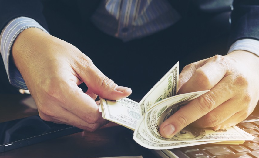 Empresário contando notas de dólar ao lado de um notebook, simbolizando os resultados financeiros positivos gerados por uma estratégia de branding bem-sucedida.
