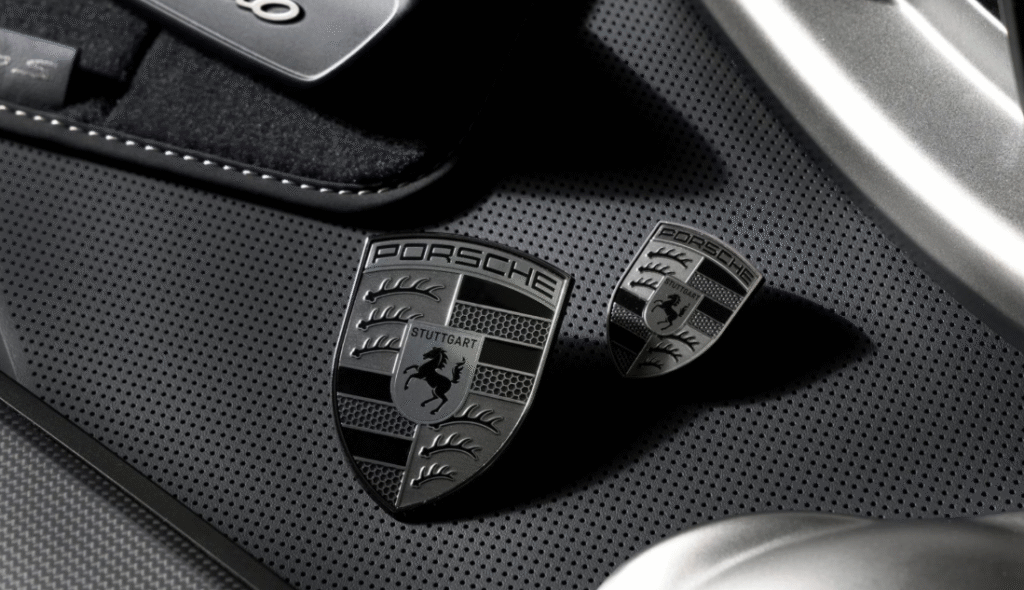 Emblemas da Porsche em preto e prata sobre superfície texturizada, simbolizando o poder do branding de luxo e a identidade visual marcante da marca automotiva.