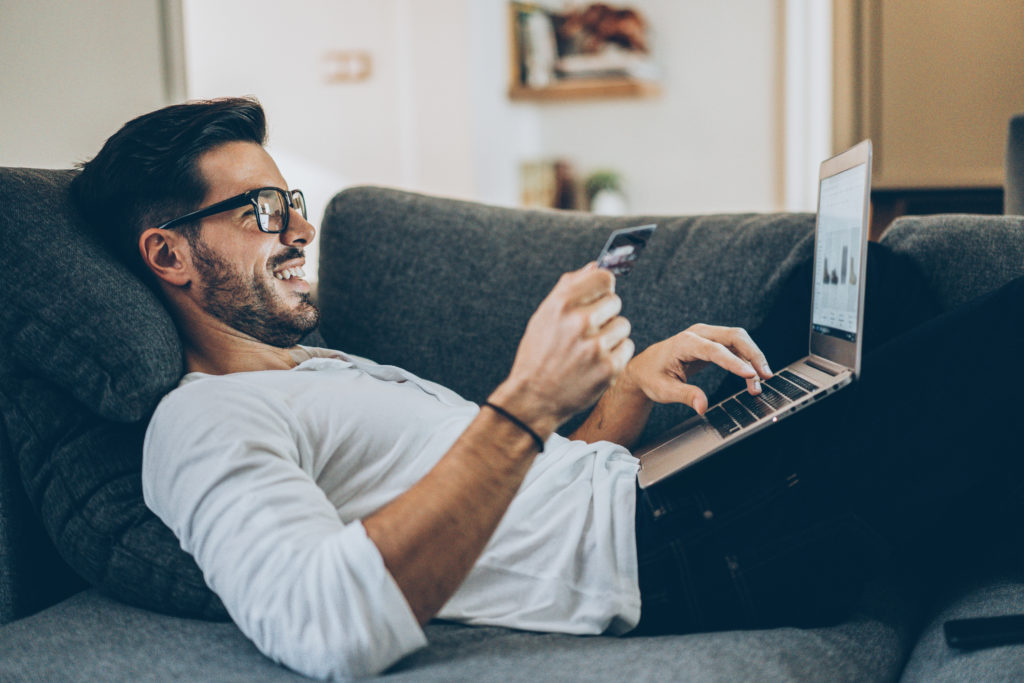 Pessoa realizando uma compra online com laptop e cartão de crédito, em um ambiente confortável. Isso simboliza a fluidez da jornada do cliente e a capacidade de transformar 'leads' em vendas com facilidade.