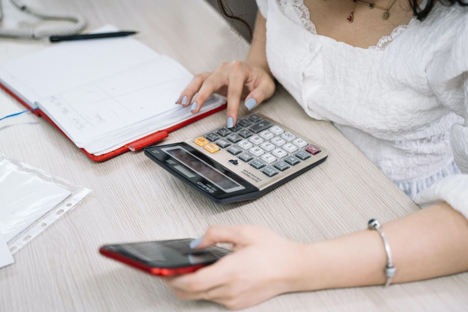 Mulher utilizando calculadora e smartphone ao lado de caderno de anotações, representando a integração de dados financeiros e ferramentas digitais no processo de automação de marketing.