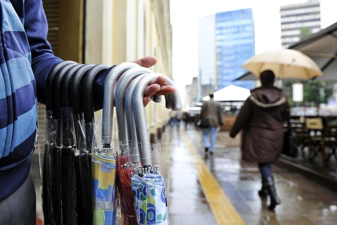 Vendedor ambulante oferece guarda-chuvas em uma rua movimentada e chuvosa, ilustrando a diferença quando alguém entende as necessidade reais na hora de vender um produto digital.