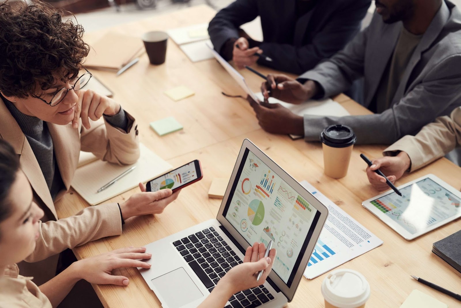 Equipe de marketing reunida em uma mesa analisando gráficos em notebook, tablet e smartphone, durante uma reunião estratégica sobre campanhas de remarketing.