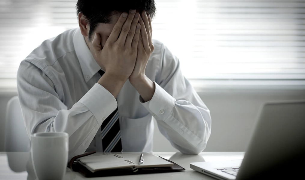 Profissional de vendas com expressão de frustração sentado à frente de um notebook, representando dificuldades na gestão do funil de vendas e conversão de leads em clientes.