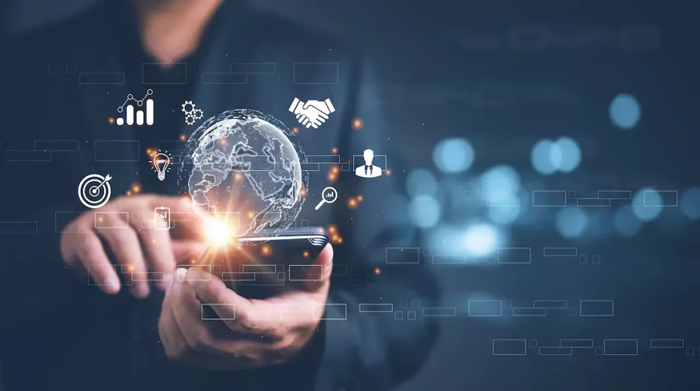 A imagem representa a essência do marketing digital, destacando a conexão global proporcionada pelos dispositivos móveis e a integração de dados, estratégias e tecnologia. Ícones de análise, networking e inovação ilustram como as empresas utilizam o marketing digital para criar campanhas inteligentes, gerar engajamento e alcançar mercados em escala mundial.