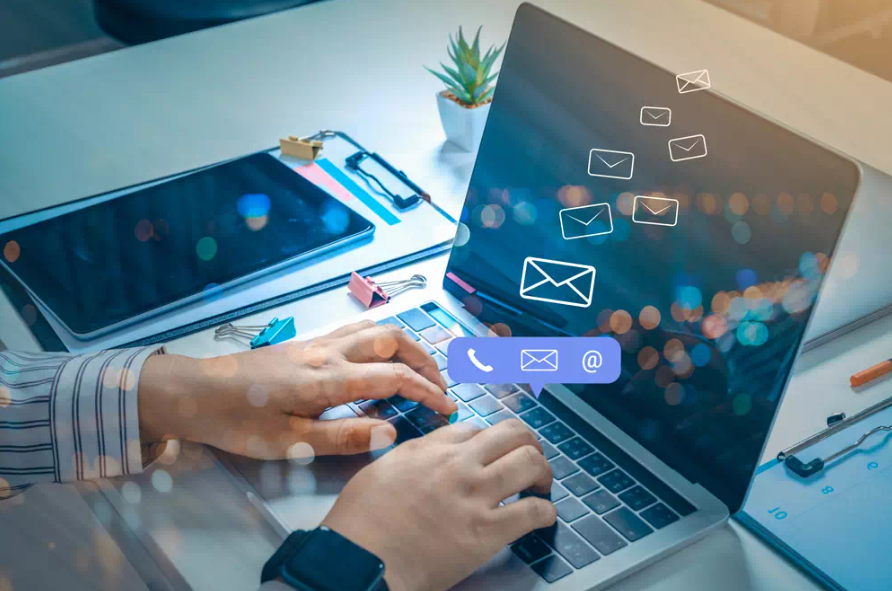 Pessoa digitando em laptop com ícones de e-mails flutuando, simbolizando estratégias de comunicação digital e e-mail marketing.