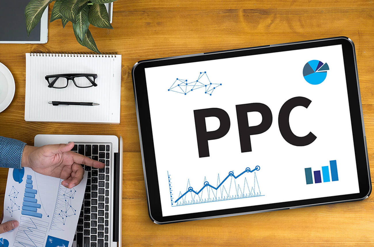Mesa de trabalho com elementos de escritório e um tablet exibindo 'PPC' e gráficos de performance. Isso simboliza a otimização e o monitoramento contínuo de campanhas de PPC para melhores resultados.