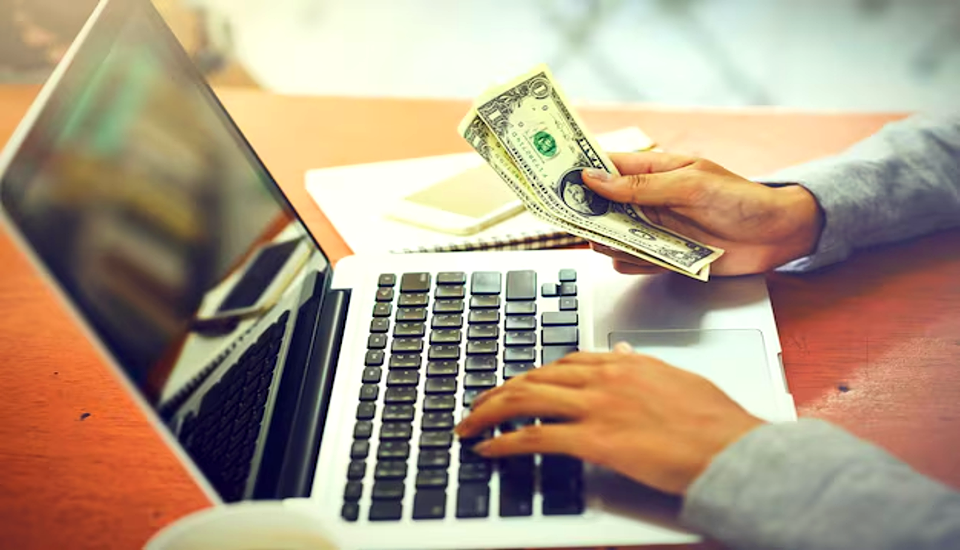 A imagem de alguém trabalhando em um laptop e manuseando dinheiro, destaca o lado financeiro do empreendedorismo digital. Isso sugere que o conteúdo aborda como os 'leads' são essenciais para o sucesso, representando oportunidades de negócio que, quando bem gerenciadas, se convertem em receita, impulsionando o crescimento financeiro.