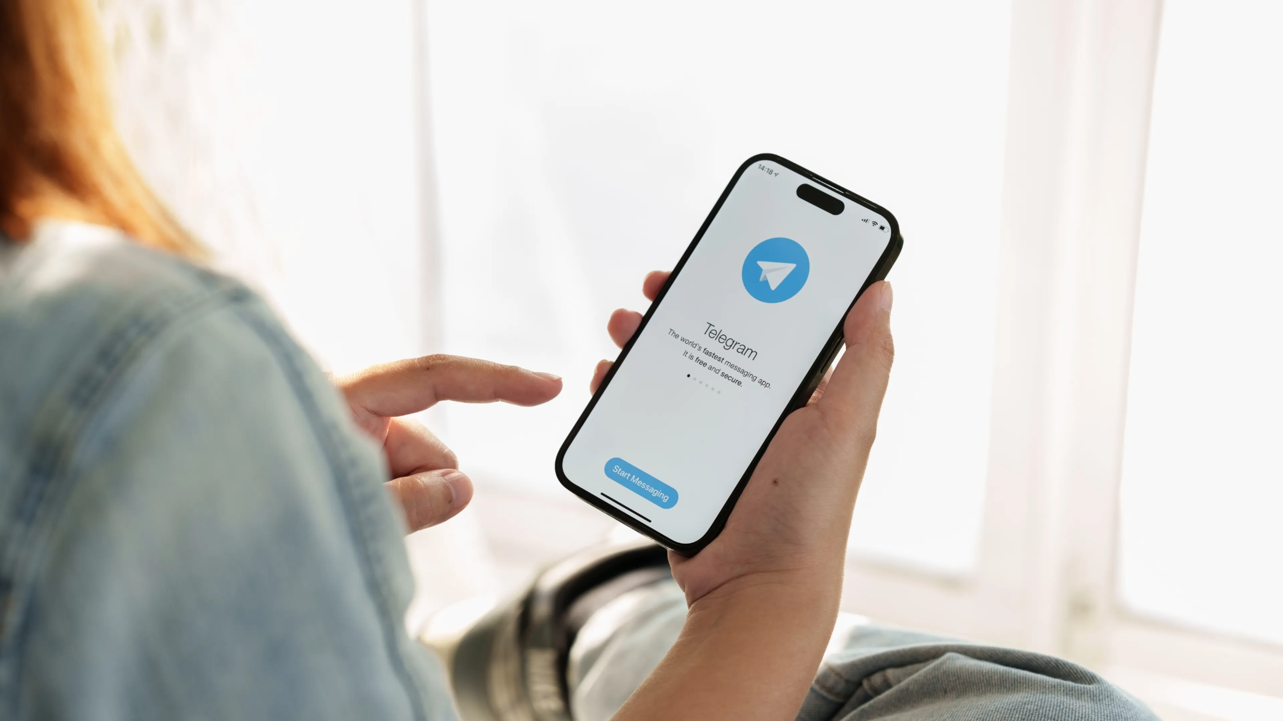 Uma mão segura um smartphone exibindo o logotipo do Telegram e uma imagem de uma mulher sorrindo. Ao lado, o nome "Telegram" em letras brancas sobre um fundo azul. A imagem representa o uso do Telegram para vendas.