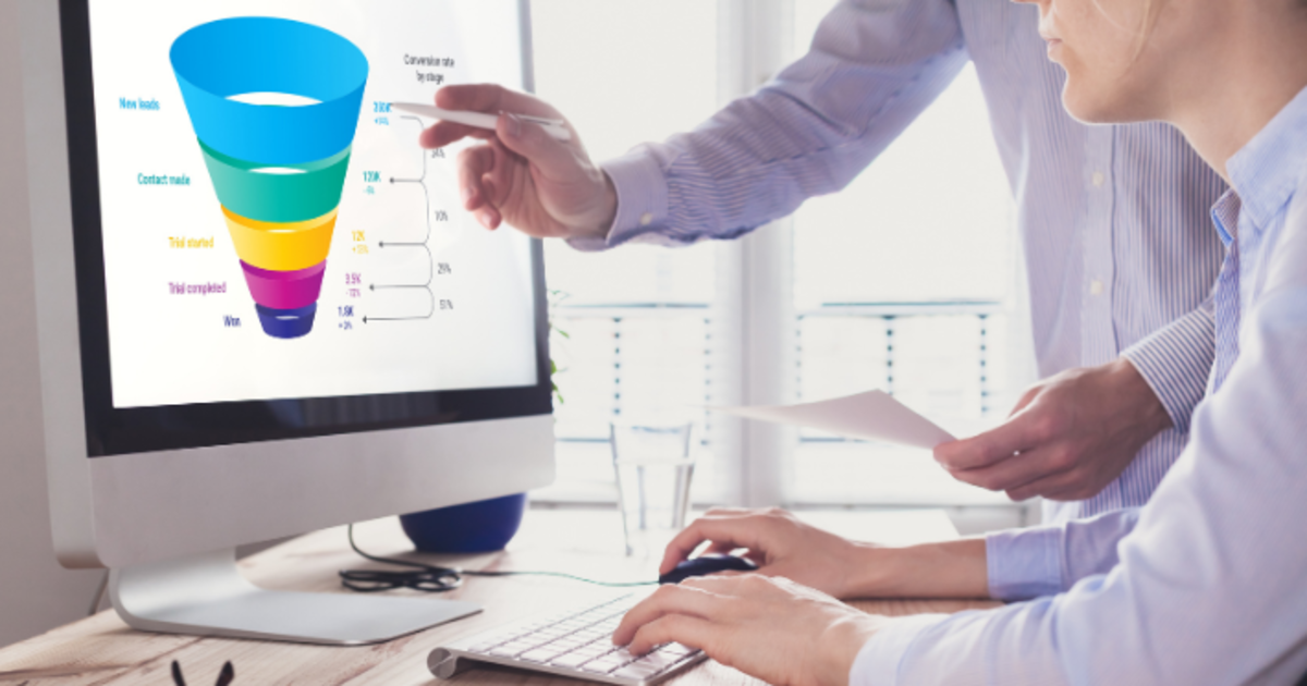Profissionais analisando um gráfico de funil de vendas em um monitor, avaliando taxas de conversão e o impacto de uma oferta Tripwire nas etapas iniciais da jornada do cliente.