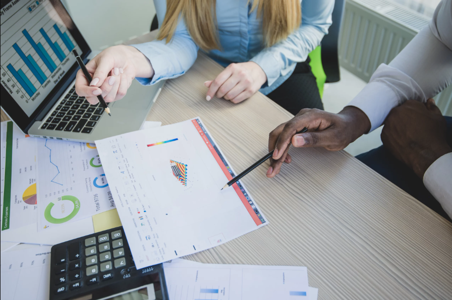 Profissionais analisando gráficos e relatórios financeiros em uma mesa de trabalho, discutindo os resultados de uma campanha com estratégia Tripwire para aumentar conversões.