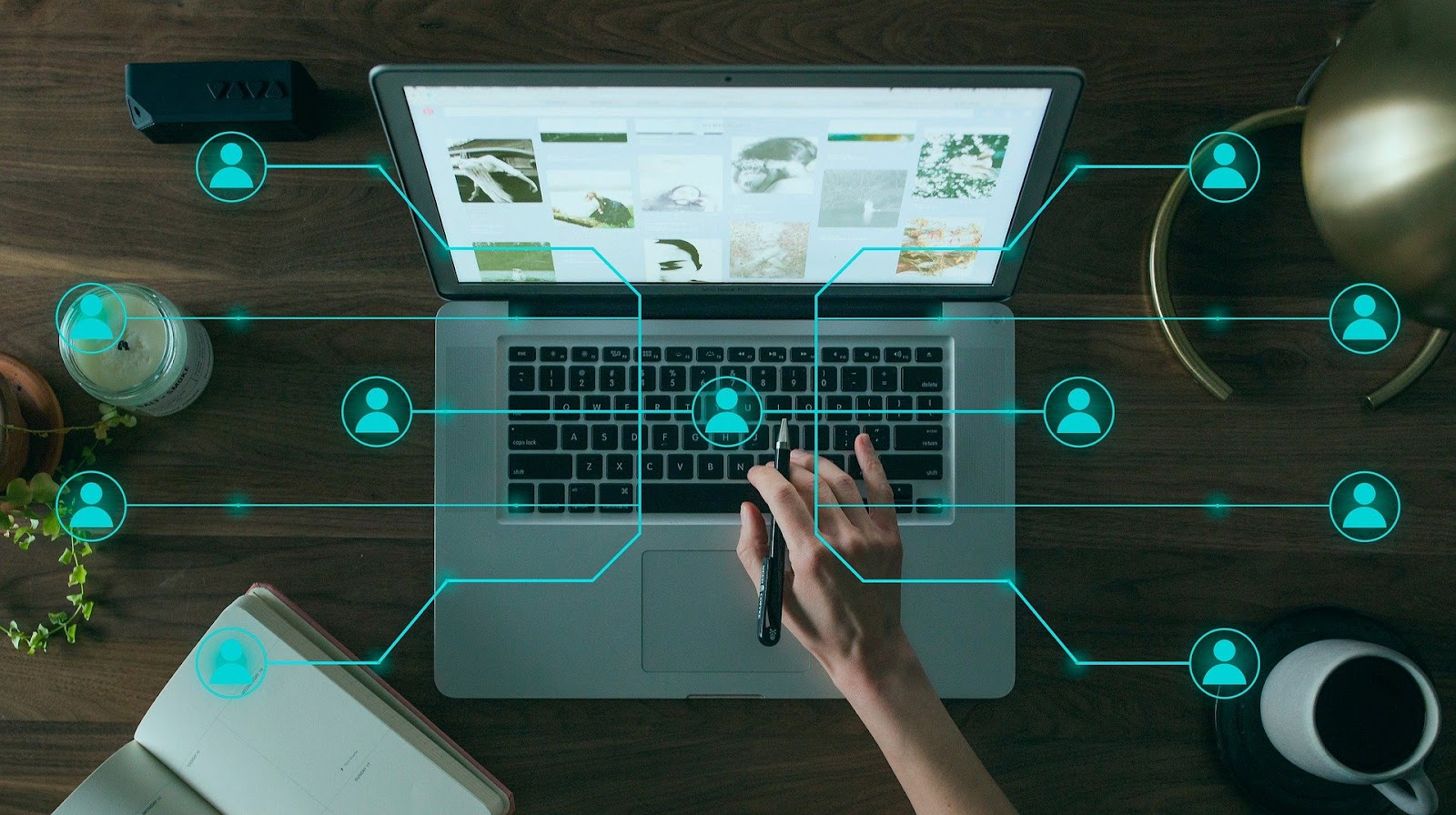 Uma pessoa interagindo com um laptop em uma mesa de madeira, onde a tela do computador exibe uma galeria de imagens. Linhas e ícones de perfil de usuário em azul neon se estendem da pessoa no teclado para diferentes pontos na tela e ao redor do laptop, simbolizando a interação e a conexão com diversos usuários. A imagem representa a distribuição e o alcance de Mini Produtos Digitais para uma audiência conectada.